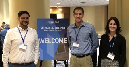 Three people standing in front of a welcome sign at a conference