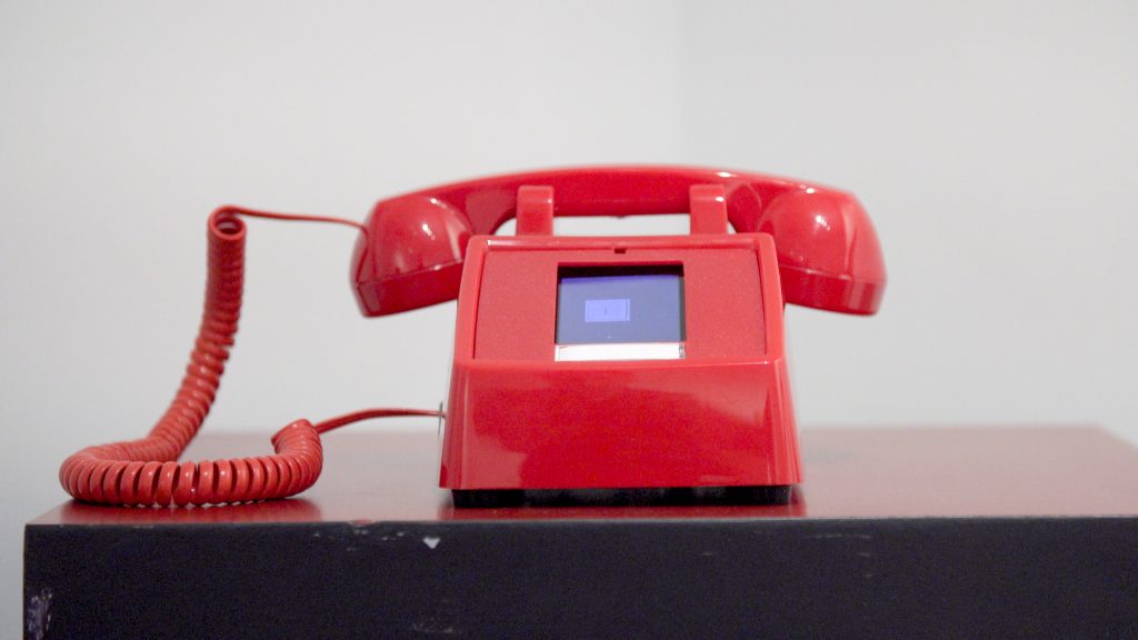 A vintage, red dial phone with a touch screen in place of the rotary dial
