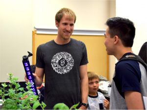 Scientist holding a black light over a plant and talking with another person