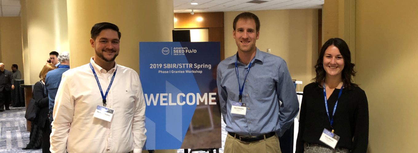 Three people standing in front of a welcome sign at a conference