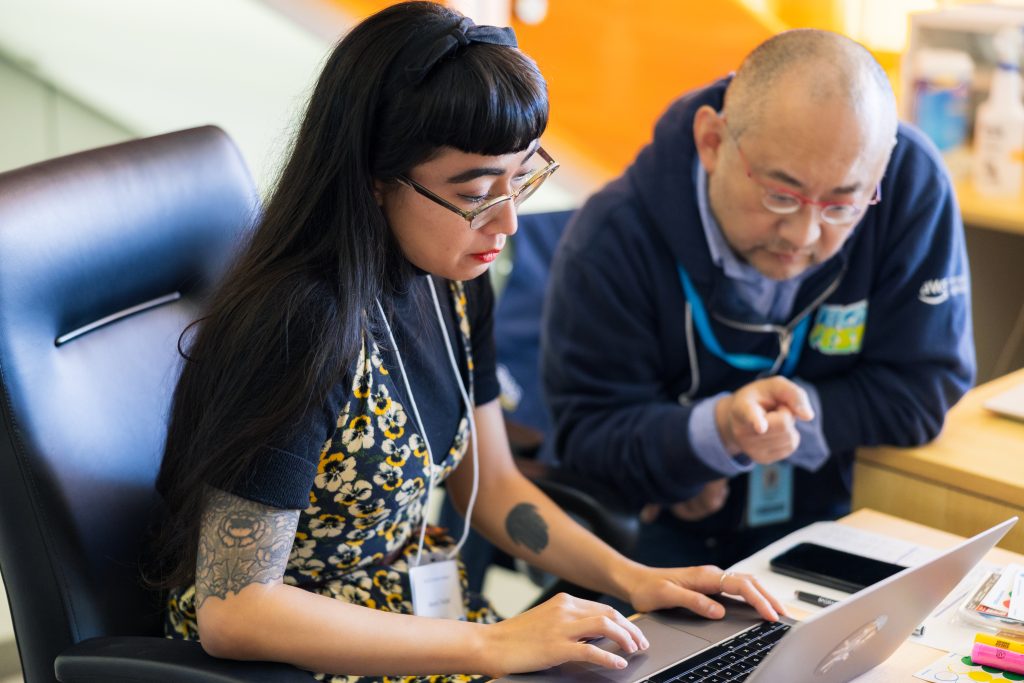 Marena Trinidad working on a laptop and talking with Robert Wang of Amazon Web Services