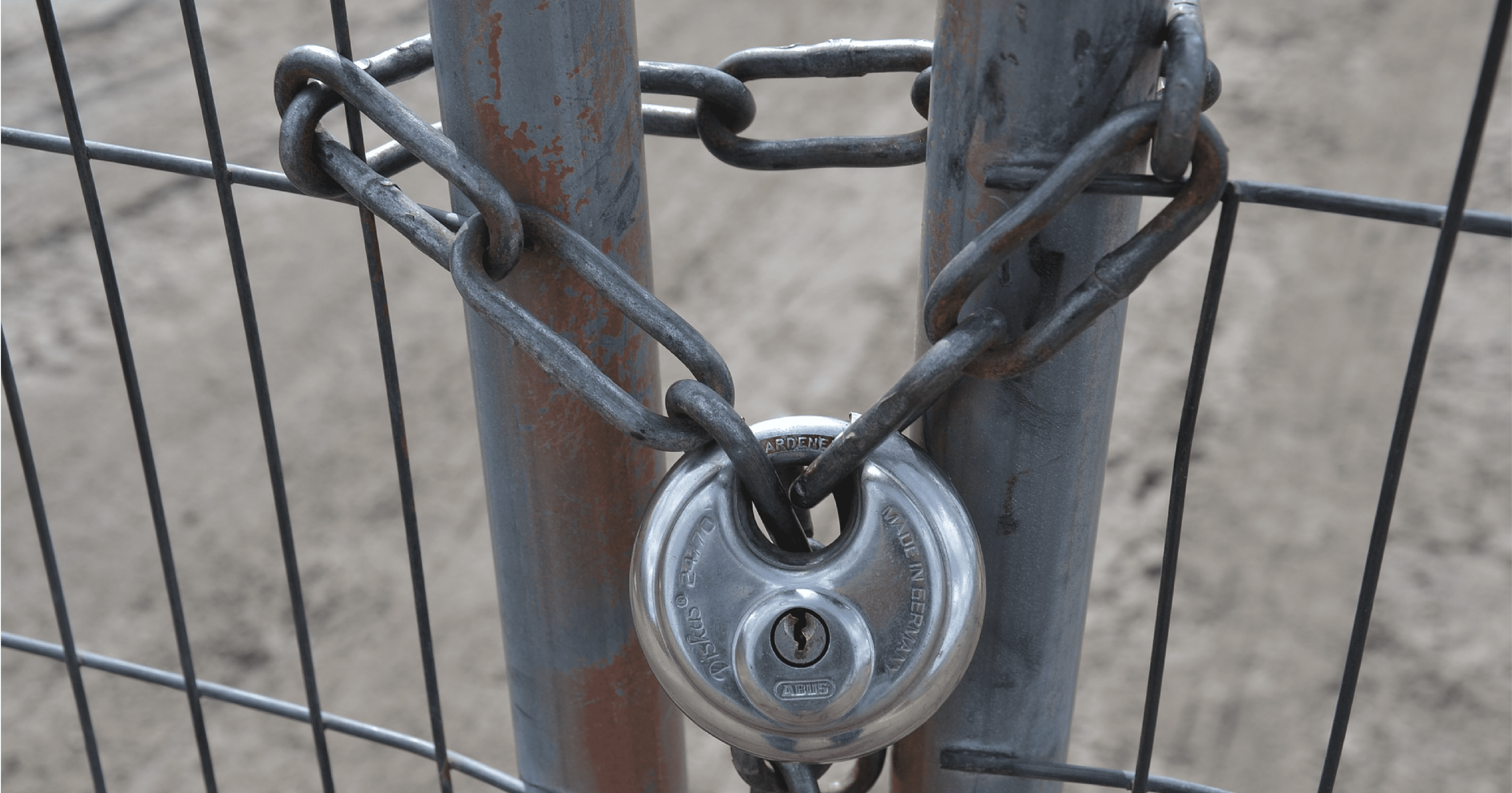 A chain link looped through a fence an secured by a lock