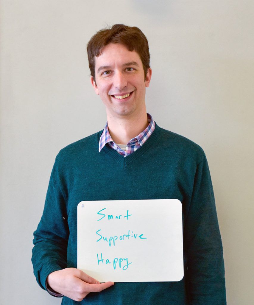 Peter Turnbaugh holding a whiteboard that says smart, supportive, happy