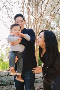 Matt Kan with his wife and infant son. They are outside on a sunny day and everyone is smiling.