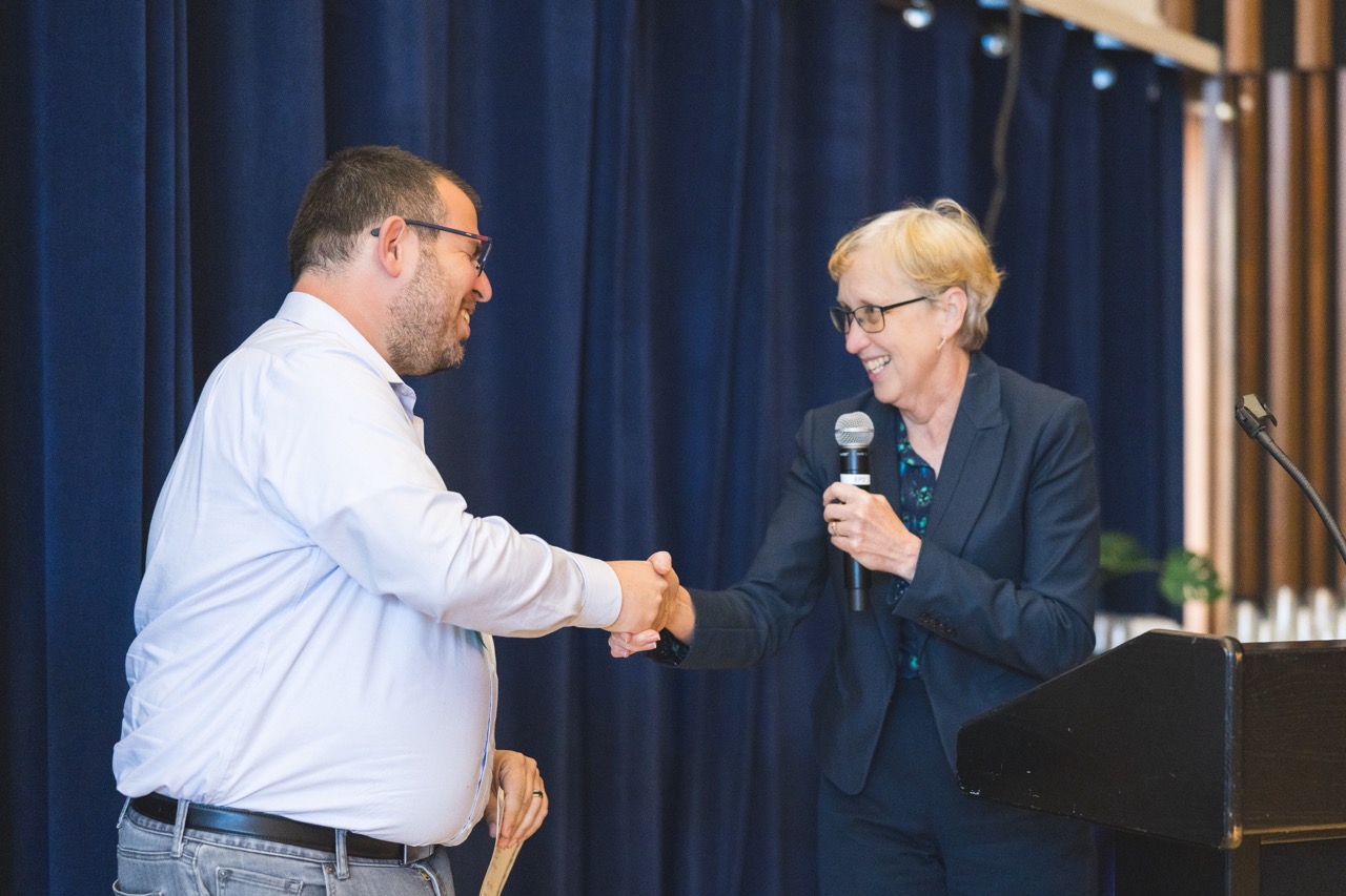 Dror Assa shakes Vice Chancellor Kathy Yellick's hand as he receives first prize in the Inside IGI 2024 poster conference.